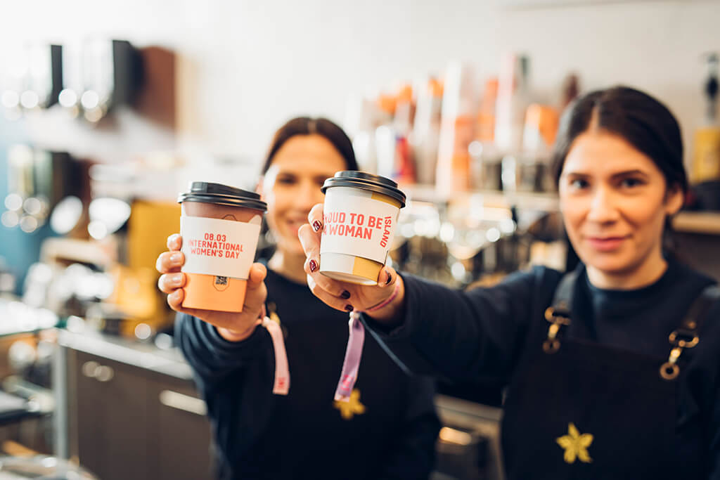Coffee Island's baristi holding coffee cups with IWD coffee sleeve and wearing IWD bracelets.