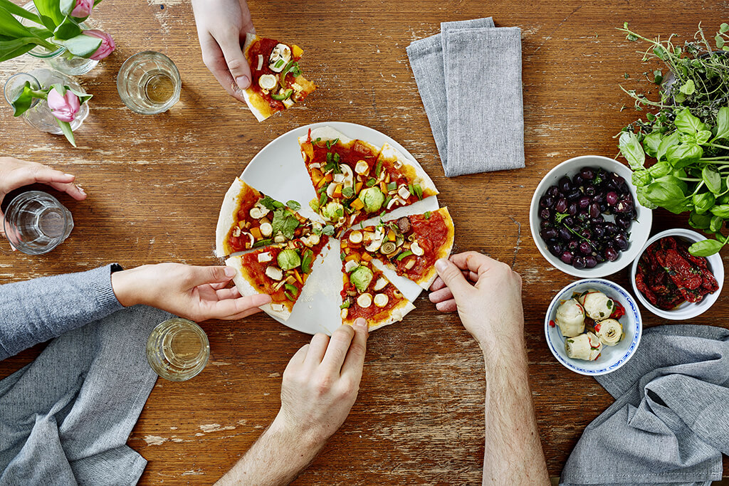 A group of people eating and enjoying a vegan/vegetarian pizza.